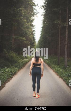 Brünette im Alter von 20-25 Jahren in schwarzer Sportbekleidung, die in der Abendsonne in der Natur läuft. Aktiver Lebensstil. Outdoor-Sport. Stockfoto