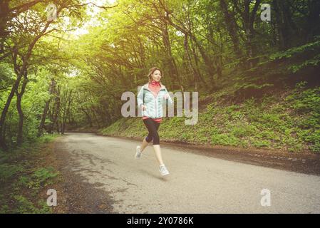 Junge Fitness blonde Frau in Kopfhörer läuft am Morgen kaukasischen Wald Trail in Sonnenlicht Stockfoto