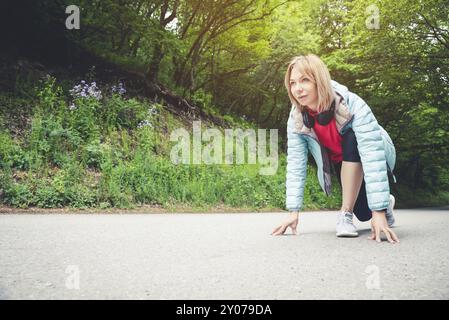 Athletische Frau läuft auf dem Land Straße. Fitness-Lauferin in bereit Startlinie Pose im Sommer Sprint Herausforderung Stockfoto