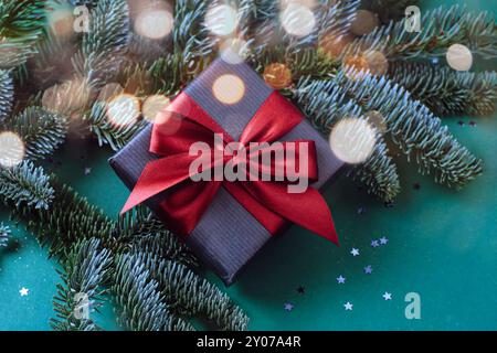 Geschenkbox mit roter Schleife und Tannenzweigen auf grünem Hintergrund mit goldenem Glitzer. Draufsicht, flach, Kopierbereich. Stockfoto