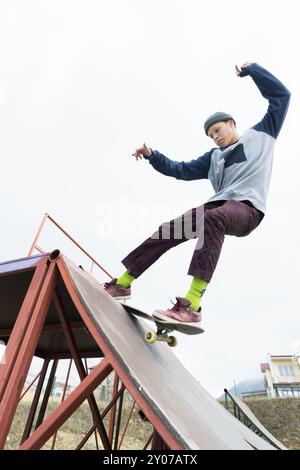 Teenager Skater in Hoodie Sweatshirt und Jeans gleiten über ein Geländer auf einem Skateboard in einem Skatepark, Weitwinkel Stockfoto