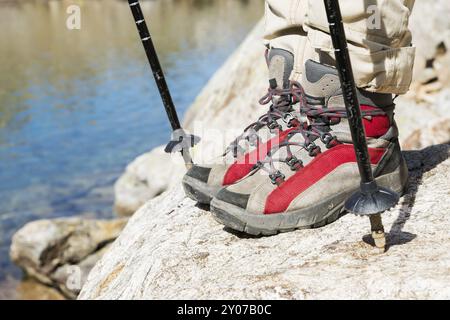 Ein schlankes, hübsches Mädchen-Hipster in einer Mütze und einer roten Jacke mit Stöcken für Nordic Walking mit Rucksack und einem gefalteten Teppich zum Entspannen steht in der mou Stockfoto