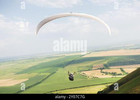 Professioneller Gleitschirm im Kokon-Anzug fliegt hoch über dem Boden gegen den Himmel und die Felder Stockfoto