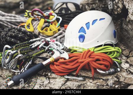 Gebrauchte Kletterausrüstung, Karabiner ohne Kratzer, Kletterhammer, weißer Helm und graues, rotes, grünes und schwarzes Seil am Stein Stockfoto