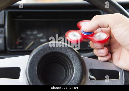 Nahaufnahme eines Mannes, der mit einem Spinner spielt, während er in einem Stau sitzt, auf dem Hintergrund des Lenkrads eines beliebten Fidget-Spinner-Spielzeugs im Auto Stockfoto