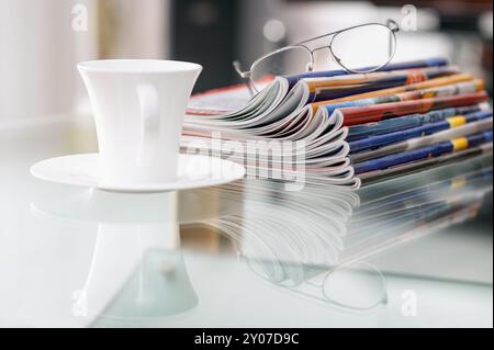 Stillleben mit Zeitschriften, Kaffeetasse und Gläsern auf einem Couchtisch Stockfoto