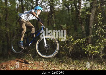 Ein junger Fahrer mit Helm fliegt auf einem Fahrrad, nachdem er von einem Hochkicker auf einem Waldradweg gesprungen ist. Aufnahmen mit Kabel für lange Belichtungsdauer Stockfoto