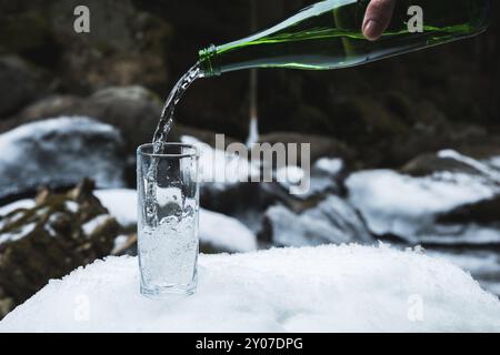 Mineralwasser wird aus einer glasgrünen Flasche in ein klares Glas-Becherglas gegossen. Ein Glas steht im Schnee. Vor dem Hintergrund eines Winters Stockfoto