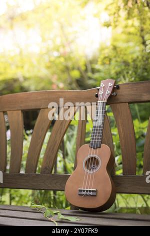 Ukulele auf einer hölzernen Parkbank im Sommer, Grünfläche im verschwommenen Hintergrund Stockfoto