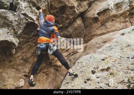 Hipster, Kletterer im Alter, in dem man einen wunderschönen Felsen ohne Versicherung und Helm hochklettert. Ein Bergsteiger in Hut und Daunenjacke mit Tasche für magnes Stockfoto