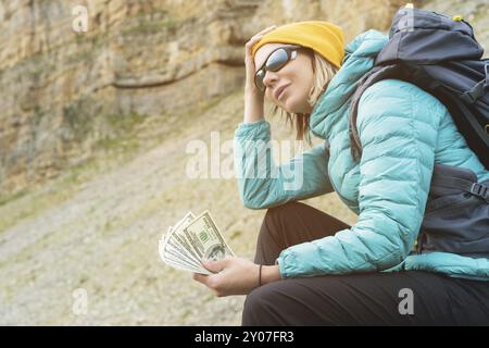 Ein Reisemädchen mit Hut und Sonnenbrille hält hundert Dollar Scheine in den Händen eines Fans vor dem Hintergrund der Klippen in der Natur. Behalten Sie Ihr HE Stockfoto