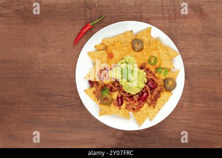 Ein Foto von Nachos mit Käse, Chili con Carne und Guacamole, traditionellen Mexikanischen Imbiss, auf einem dunklen Hintergrund mit rotem Pfeffer und Kopieren sp Stockfoto