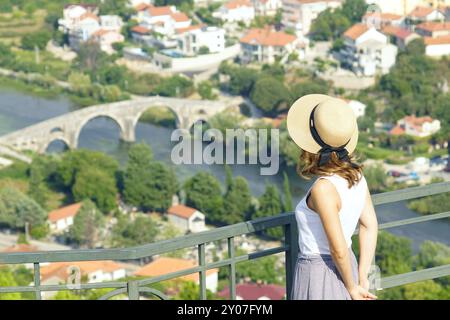 Eine Frau steht auf der Aussichtsplattform des Klosters Hercegovacka Gracanica und blickt auf die Landschaft mit der Brücke Arslanagica (Trebinje) Stockfoto