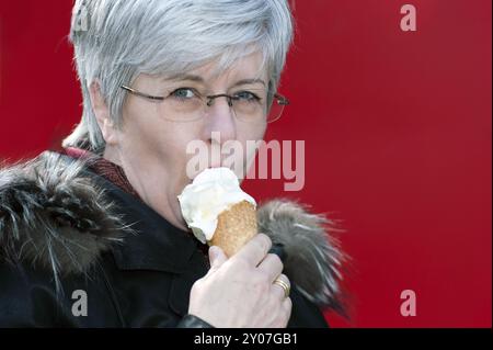 Frau steht vor einer roten Wand und isst Eis Stockfoto