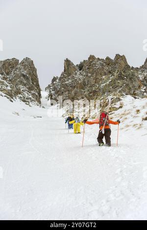 Extremskifahrer und Snowboarder klettern auf den Gipfel entlang des Couloirs zwischen den Felsen, bevor die Freeride-Abfahrt im Hinterland stattfindet. Das Konzept einer Gruppe e Stockfoto