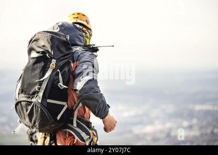 Nahaufnahme eines Kletterers in Ausrüstung und mit Rucksack mit Ausrüstung am Gürtel, steht auf einem Felsen, in großer Höhe Stockfoto
