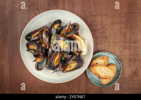 Marinara Muscheln, Moules Mariniere, Overhead shot auf einem dunklen Holzmöbeln im Landhausstil Hintergrund mit geröstetem Brot und Copyspace Stockfoto