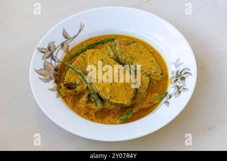 Leckeres Shorshe auf einem weißen Teller auf einer hellen hölzernen Oberfläche. Dieses Rezept wird aus Hilsa-Fisch (Tenualosa ilisha) hergestellt. Traditionelle bengalische Küche Co Stockfoto