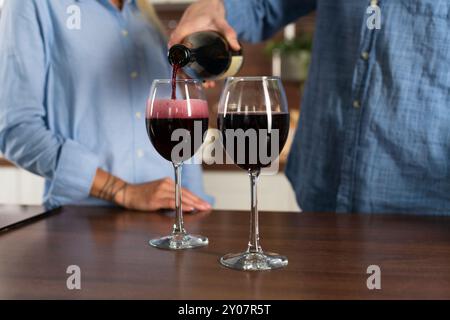 Nicht erkennbarer Mann, der einen Rotwein in ein Glas in Blasen mit einem Spritzer auf dem Tisch in der Küche eingoß, Nahaufnahme Stockfoto