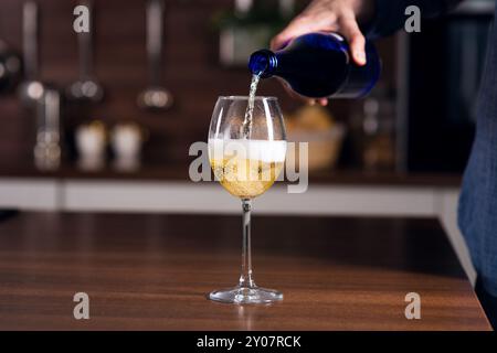 Nicht erkennbarer Mann, der in ein Weißweinglas in Blasen gegossen wurde, mit einem Spritzer auf dem Tisch in der Küche, Nahaufnahme Stockfoto