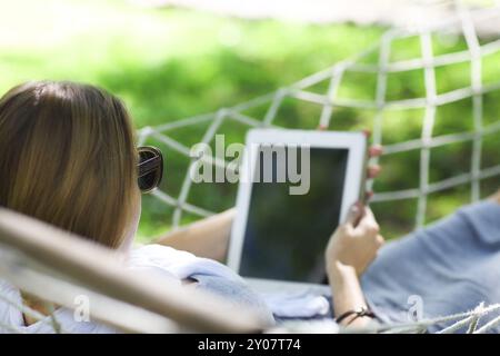 Zeit zum Faulenzen. Frau mit Hut in der Hängematte mit Tablet-Computer an einem Sommertag Stockfoto