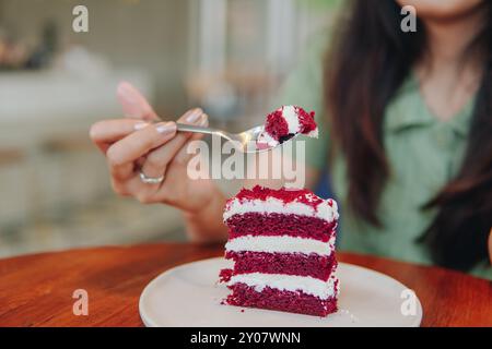 Die Hand einer Frau hält einen Löffel und isst ein Stück roter Samtkuchen mit verschwommenem Café-Hintergrund. Stockfoto