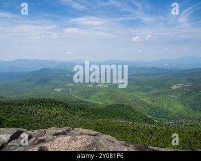 Atemberaubende Aussicht vom Gipfel des Cascade Mountain, mit einem zerklüfteten Felsen im Vordergrund und dem olympischen Skisprung Komplex, der in der Ferne in La sichtbar ist Stockfoto