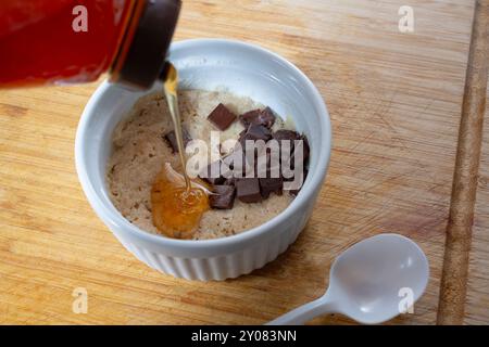 Ein Blick auf eine Flasche Honig, die in einem Ramekin in einen Mikrowellenkeks fließt. Stockfoto