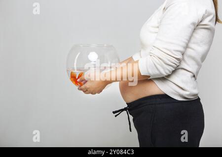 Glücklich schwanger Frau ein Goldfischglas mit einem Goldfisch in ihren Händen hält. Pflege und Liebe Konzept Stockfoto