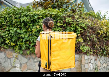 Das hispanische Mädchen mit einem gelben Rucksack wird von hinten gesehen, während sie geht, um ihre Aufgaben zu erfüllen. Das Bild fängt sie in Bewegung ein Stockfoto