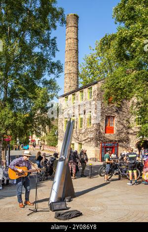 Busker und Leute am St. George's Square in der Marktstadt Hebden Bridge in West Yorkshire genießen die Sommersonne und essen draußen Stockfoto