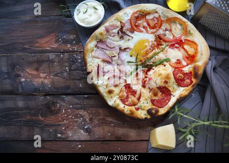 Pizza Carbonara mit Speck, Salami, Parmesan-Käse und Huhn-Ei am rustikalen Holztisch Stockfoto