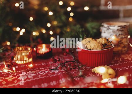 Rote festliche Schüssel voll mit leckeren Weihnachts-Schokoladenkeksen, verschwommener Hintergrund mit Weihnachtstanne Dekorationen, Lichter, Girlanden und Kerzen. Fe Stockfoto