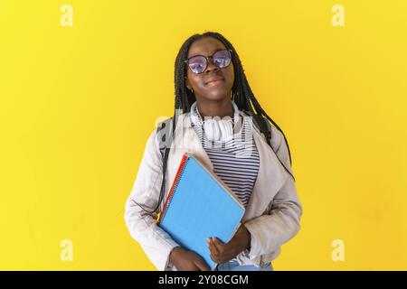 Atelierporträt mit gelbem Hintergrund eines afrikanischen jungen Universitätsstudenten mit Notizbüchern und Tasche Stockfoto