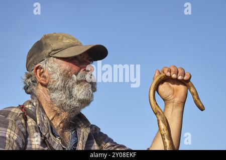 Goatherd mit Stock, ein älterer Mann mit grauem Bart und Mütze, der einen Holzstock unter blauem Himmel hält, Lefka Ori, Weiße Berge, Bergmassiv, Wir Stockfoto