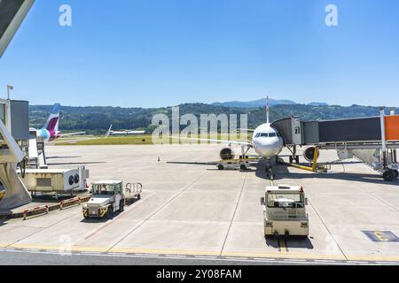 Ein großes weißes Flugzeug parkt auf dem Asphalt eines Flughafens. In der Nähe des Flugzeugs befinden sich mehrere Fahrzeuge, darunter ein LKW und ein Auto Stockfoto