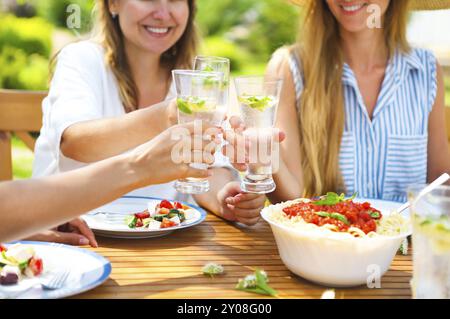 Glücklich Freundinnen mit Gläsern Limonade am Esstisch im Rasen. Nahaufnahme Stockfoto