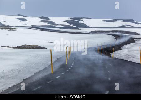 Eine Nebelspur zieht sich über eine gekrümmte Asphaltstraße durch eine verschneite Landschaft Stockfoto