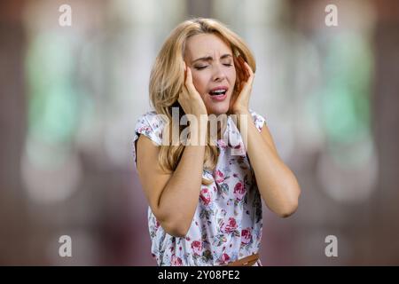 Porträt einer Reifen blonden Frau mit Kopfschmerzen. Unscharfer abstrakter Hintergrund. Stockfoto