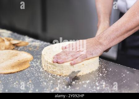 Der Konditor schneidet den Biskuitkuchen in Schichten. Kuchenherstellungsprozess Stockfoto