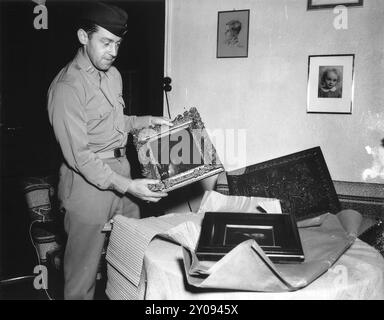 Ein US-Soldat eröffnet Pakete mit von den Nazis geplünderten Kunstwerken für die Privatsammlung von Joseph Goebbels. Er trägt das Gemälde „Mondlandschaft“ von Albert Cuyp. Auf dem Tisch liegt die „Rembrandts Mutter“ von Gerrick, einem Schüler von Rembrandt. Dahinter befindet sich ein Fresko aus dem 18. Jahrhundert, von dem angenommen wird, dass er aus einer französischen Kirche gestohlen wurde. Stockfoto