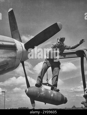 Auf einer 500-Pfund-Sprengbombe, um sie am Ende eines Krans stabil zu halten, befindet sich CPL. Lloyd Shumway, Istrouma, La., Ordnance Armament man auf einer USAAF North American P-51 Mustang Jagdstation in England, um 1944 Stockfoto