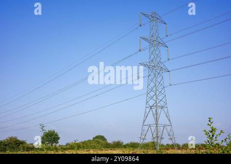 Ein Hochspannungs-Stromübertragungsturm inmitten einer offenen Landschaft unter einem klaren blauen Himmel. Stockfoto