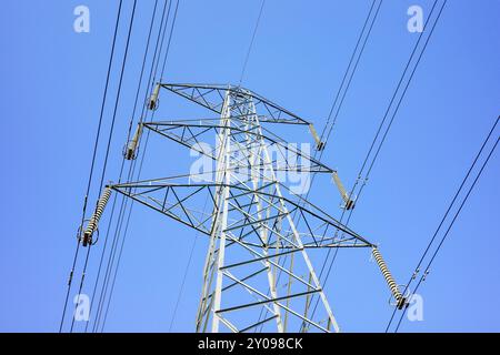 Ein hoher elektrischer Pylon aus Metall unterstützt mehrere Kabelsätze, die für die Übertragung von Elektrizität unerlässlich sind, wolkenloser klarer blauer Himmel. Stockfoto