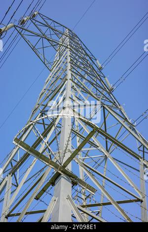 Ein hoher elektrischer Pylon aus Metall unterstützt mehrere Kabelsätze, die für die Übertragung von Elektrizität unerlässlich sind, wolkenloser klarer blauer Himmel. Stockfoto