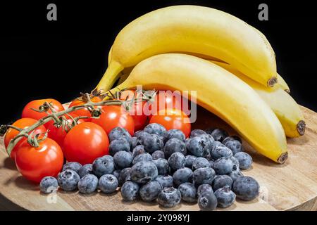 Blaubeeren, Bananen und Tomaten werden auf einem Holzbrett serviert Stockfoto