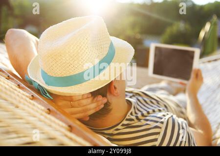 Zeit zum Faulenzen. Mann mit Hut in der Hängematte mit Tablet-Computer an einem Sommertag Stockfoto