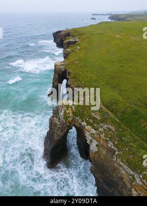 Steile Küste mit charakteristischen Felsbögen und tosenden Wellen, die gegen die Felsen krachen, aus der Vogelperspektive, Praia das Catedrais, Playa de las Catedr Stockfoto