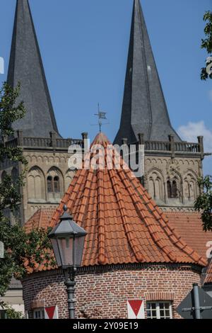 Gebäude mit rotem Ziegeldach und zwei Kirchtürmen im Hintergrund unter blauem Himmel, Straßenlaterne im Vordergrund, Xanten, Niederrhein, Nordrhein Stockfoto