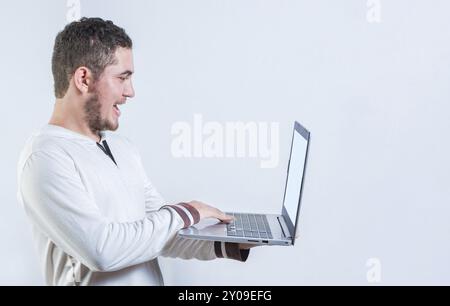 Porträt eines glücklichen jungen Mannes, der mit einem Laptop isoliert steht. Ein aufgeregter Kerl, der eine Werbeaktion auf dem Laptop-Bildschirm ansieht Stockfoto